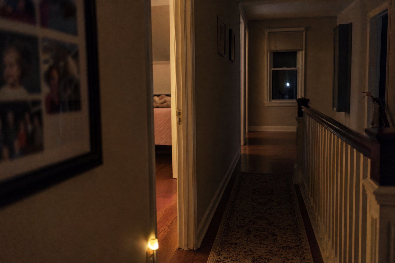 A dim upstairs hallway at night with a nightlight and a door left ajar