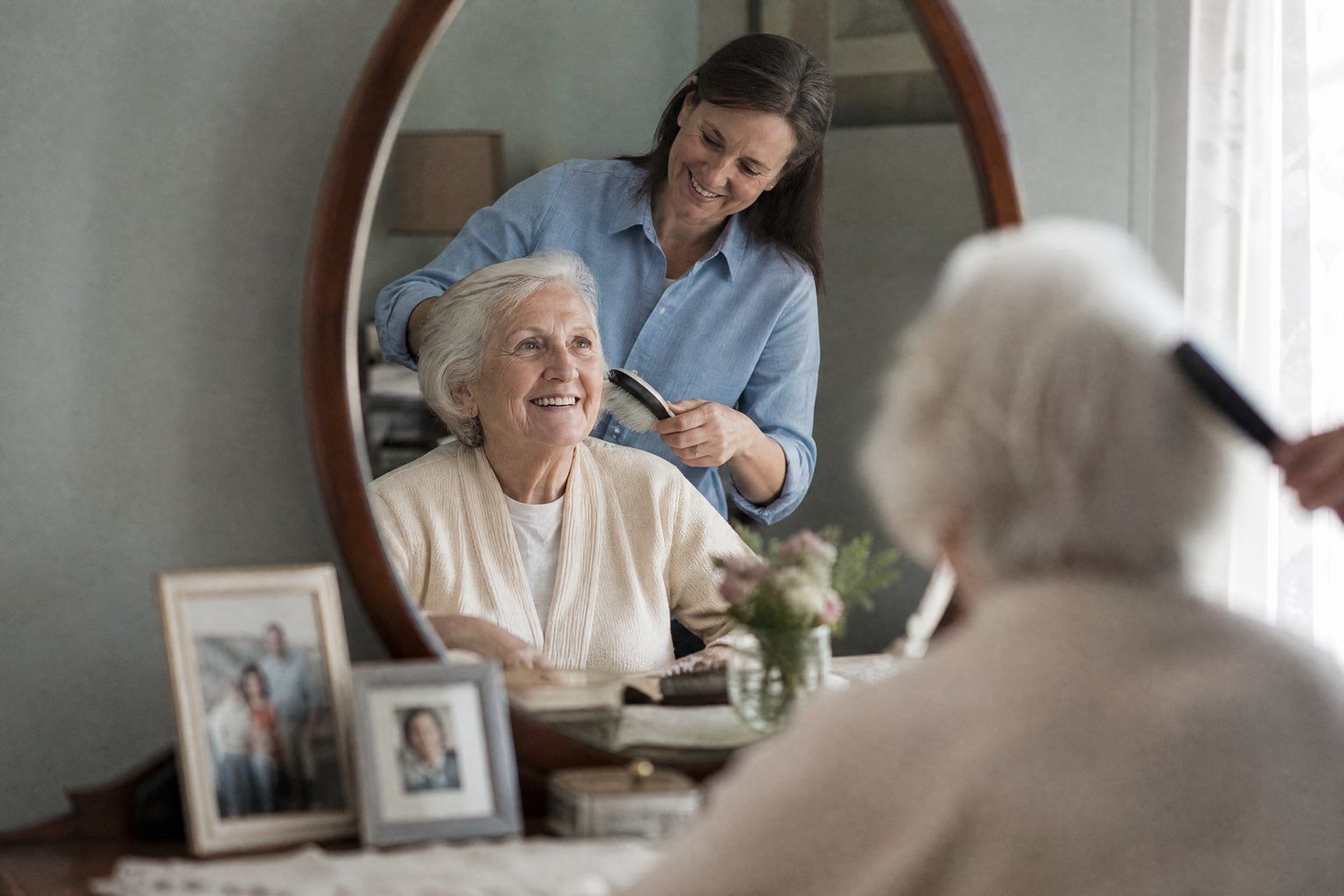 A caregiver brushing an older woman’s hair at her dresser